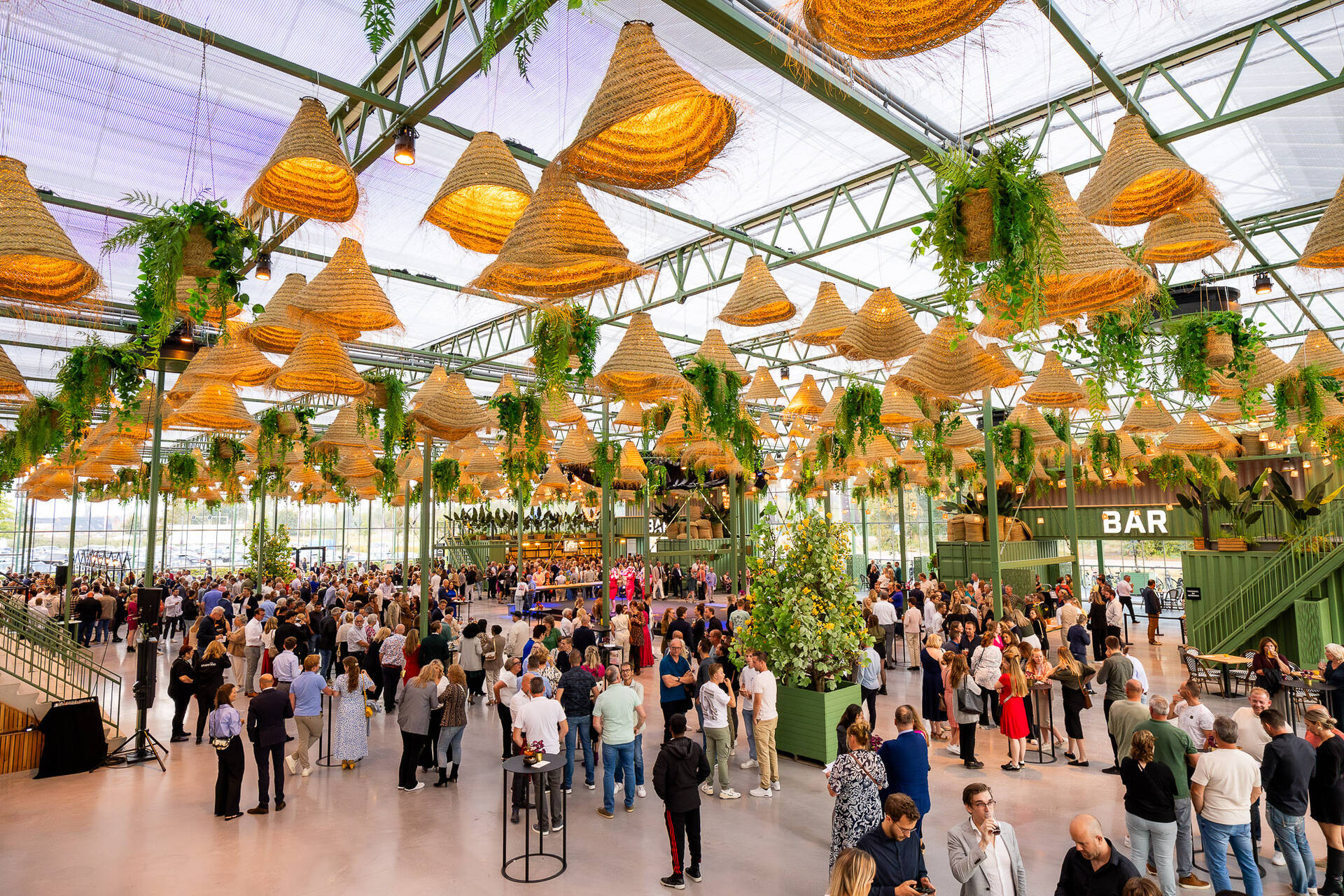 Overzichtsfoto van een evenement in de Evenementenkas van de Midden Nederland Hallen. Er staan veel mensen te borrelen en praten met elkaar.