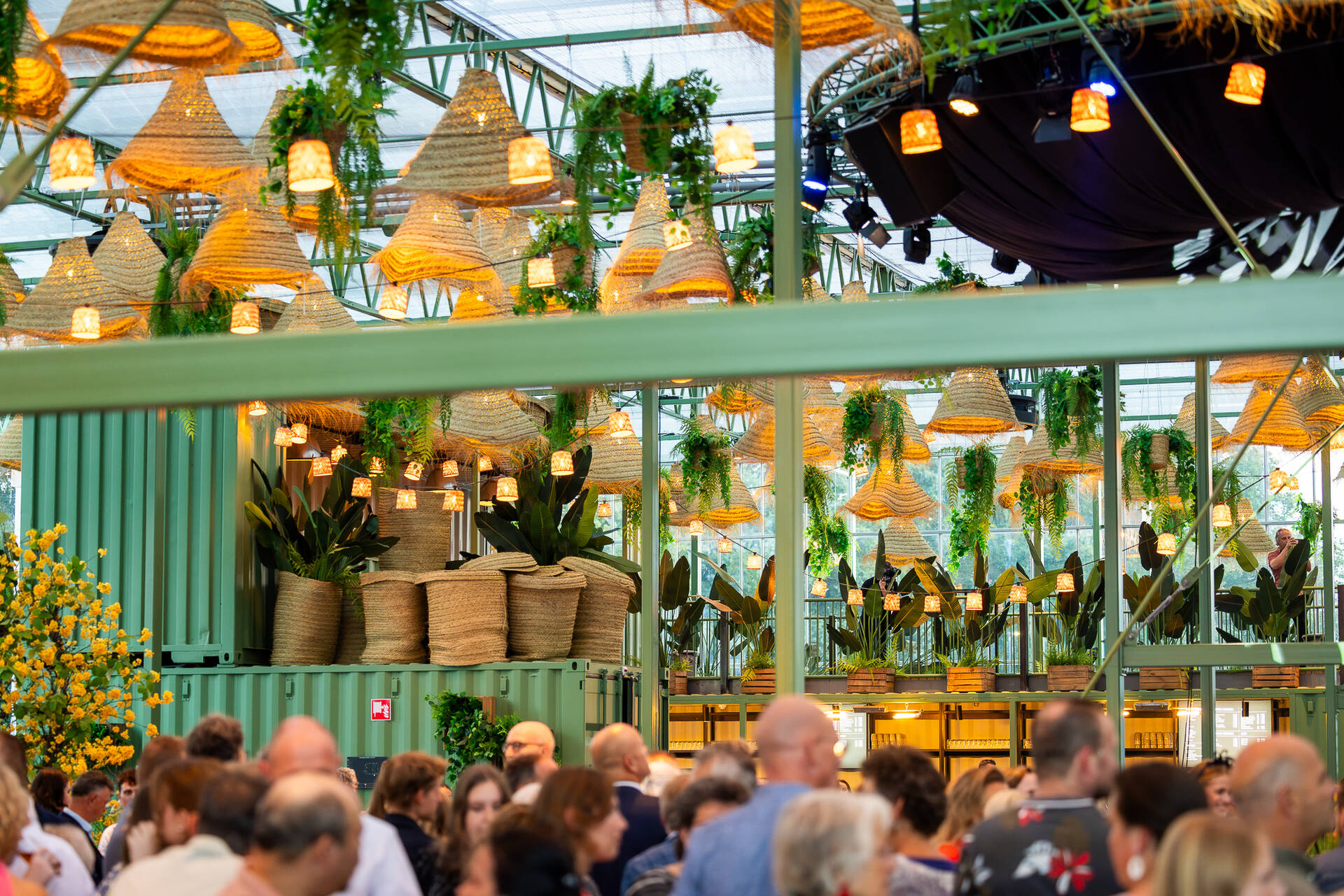 Foto in de Evenementenkas van de Midden Nederland Hallen waar een evenement bezig is. Op de voorkant staan bezoekers te borrelen, maar de focus ligt op de achtergrond waar een groene bar staat.